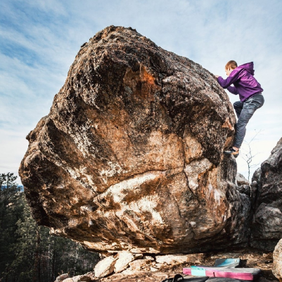 Person dressed in a hoodie sweatshirt climbs a boulder in Black Hills National Forest on a warm winter day